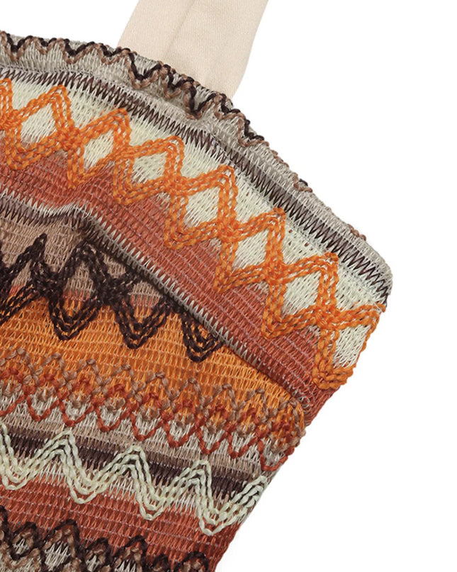 Knit tie shoulder jumpsuit close-up with orange, brown, and cream zigzag pattern. Smocked and tied details visible.